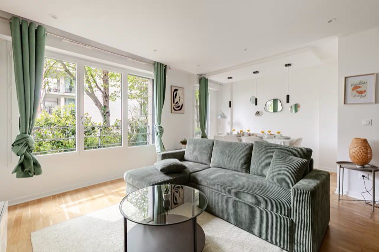 Le salon et son canapé d'angle vert devant la grande fenêtre